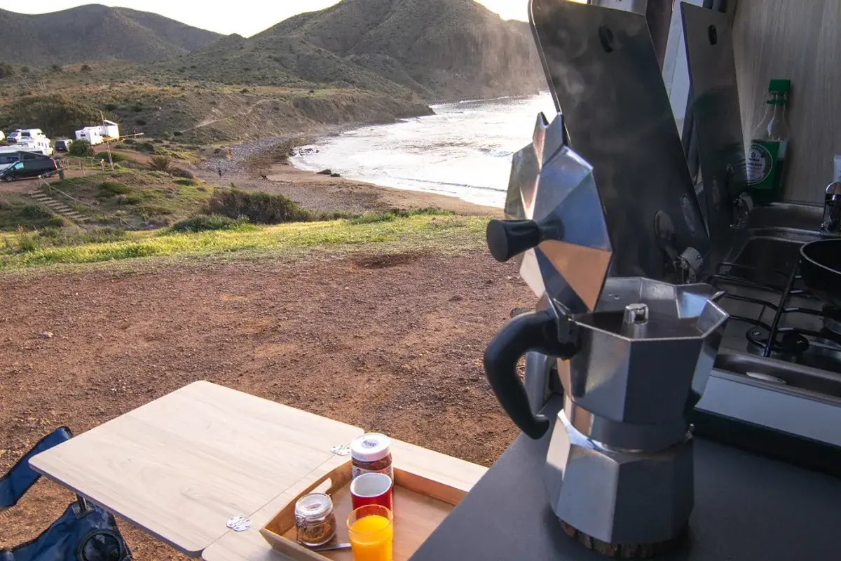 Desayuno junto a una cafetera en el interior de una camper con vistas a la costa