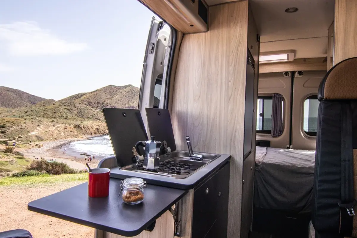 Interior de una camper de alquiler en Madrid con cocina equipada y vistas al mar desde la ventana