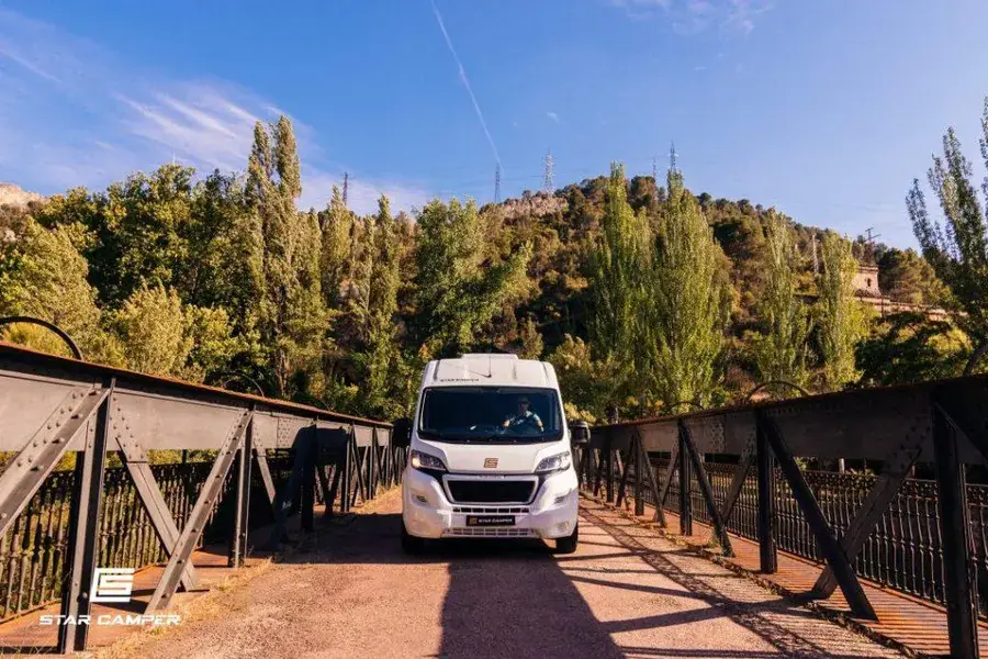 Autocaravana aparcada en zona habilitada para pernocta señalizada, rodeada de pinos