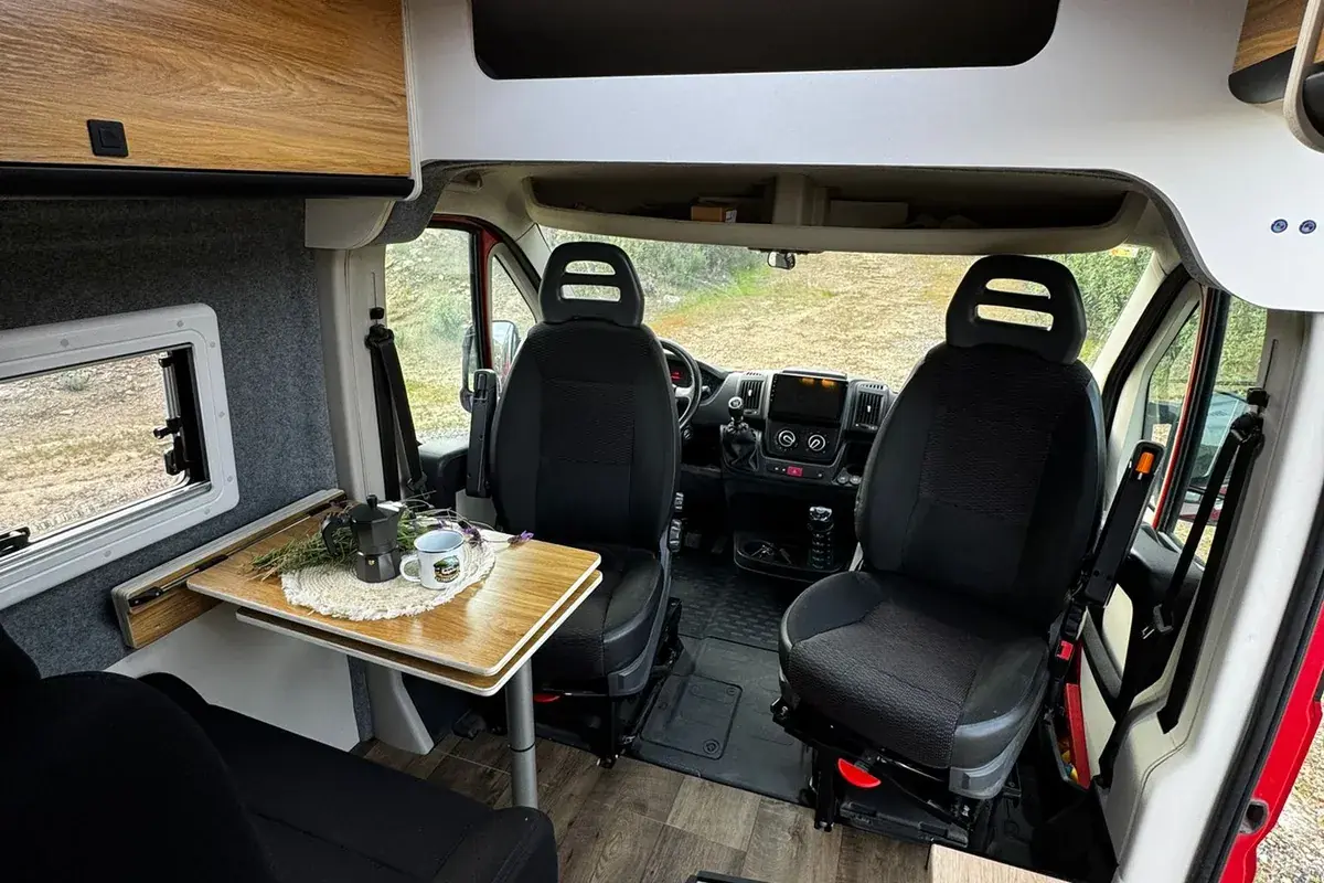 Vista interior de la cabina de una furgoneta camper con asientos y volante, lista para conducir