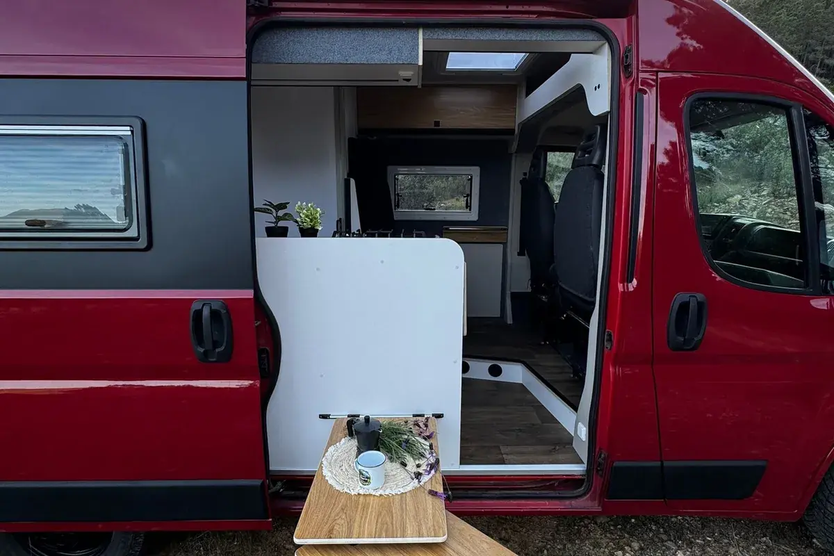 Furgoneta camper de alquiler con la puerta lateral abierta y mesa exterior desplegada